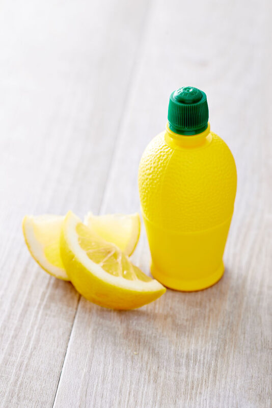 Two lemon slices placed next to a bottle of lemon juice