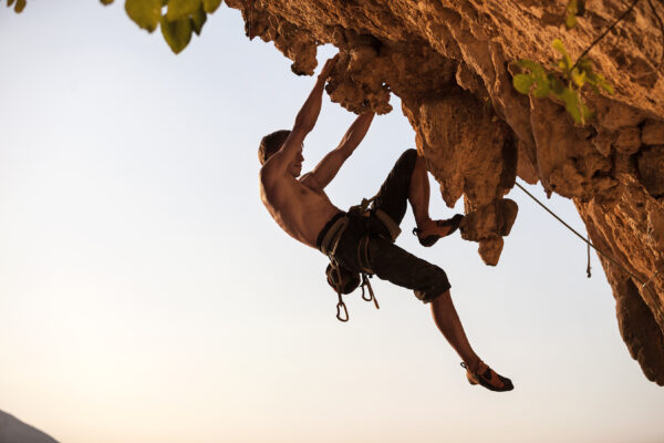 rock climber hanging off of peak at sunset